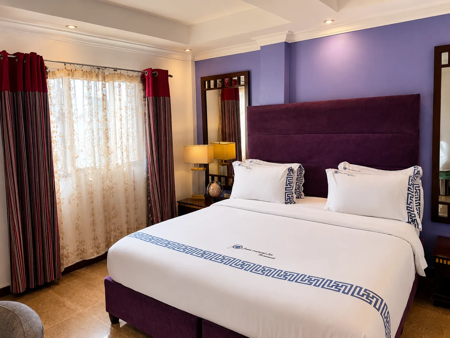 Quarto Casal Maior com cama de casal, cabeceira alta em veludo roxo, candeeiros de mesa, espelho e janela ampla