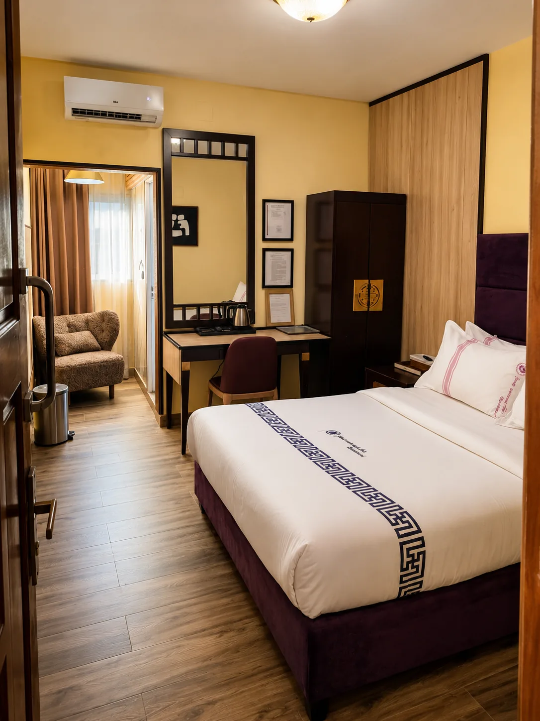Quarto com cama, parede amarela, secretária com espelho, roupeiro de madeira escura e zona de estar com poltrona junto à janela